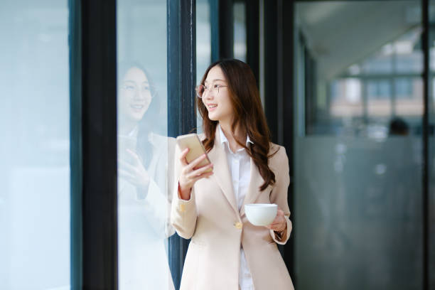 Businesswoman smiling while holding a coffee cup and checking her phone during a work break