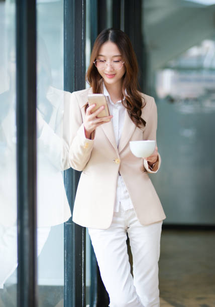 istock Businesswoman smiling while holding a coffee cup and checking her phone during a work break 2185420299