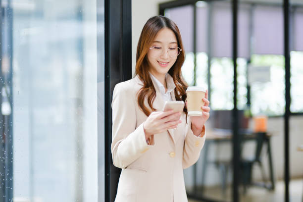 istock Businesswoman smiling while holding a coffee cup and checking her phone during a work break 2185420301