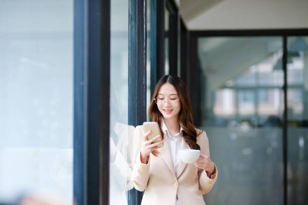 istock Businesswoman smiling while holding a coffee cup and checking her phone during a work break 2185420305