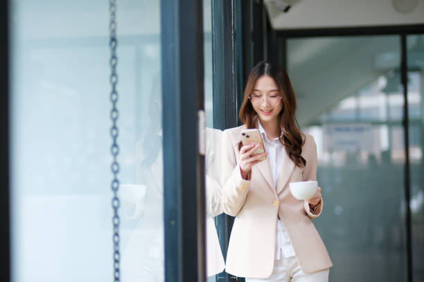 istock Businesswoman smiling while holding a coffee cup and checking her phone during a work break 2185420307