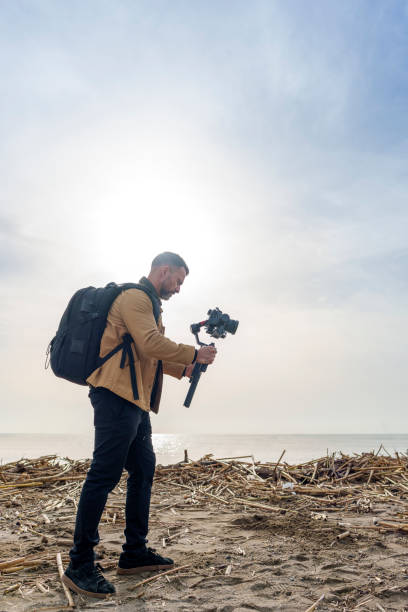 istock Camera Operator Filming Flood-Damaged Vegetation and Debris Washed Ashore on a Beach Using a Gimbal 2185422589