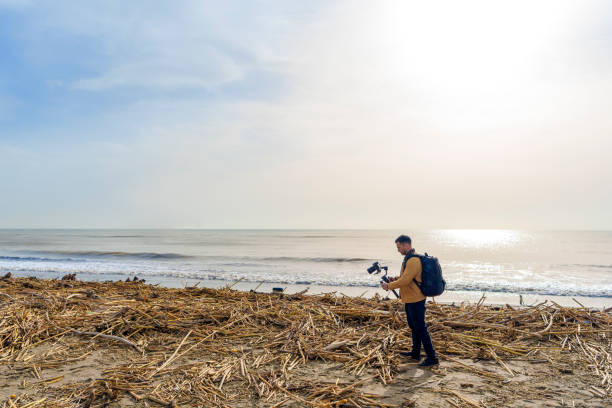 istock Camera Operator Filming Flood-Damaged Vegetation and Debris Washed Ashore on a Beach Using a Gimbal 2185422594