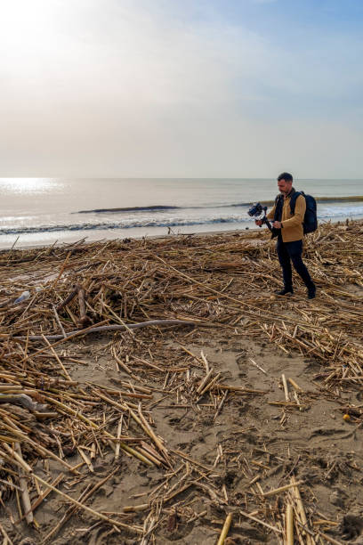 istock Camera Operator Filming Flood-Damaged Vegetation and Debris Washed Ashore on a Beach Using a Gimbal 2185422603