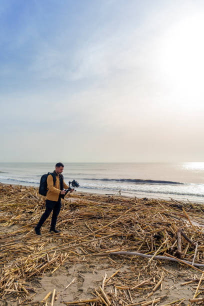 istock Camera Operator Filming Flood-Damaged Vegetation and Debris Washed Ashore on a Beach Using a Gimbal 2185422606