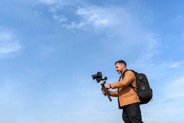 istock Male Mature Camera Operator Filming with a Gimbal Against a Clear Blue Sky Background 2185422622