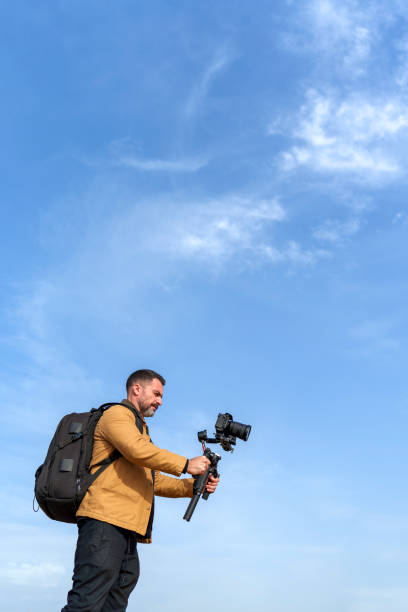 istock Mature Camera Operator Filming with a Gimbal Against a Clear Blue Sky Background 2185422628