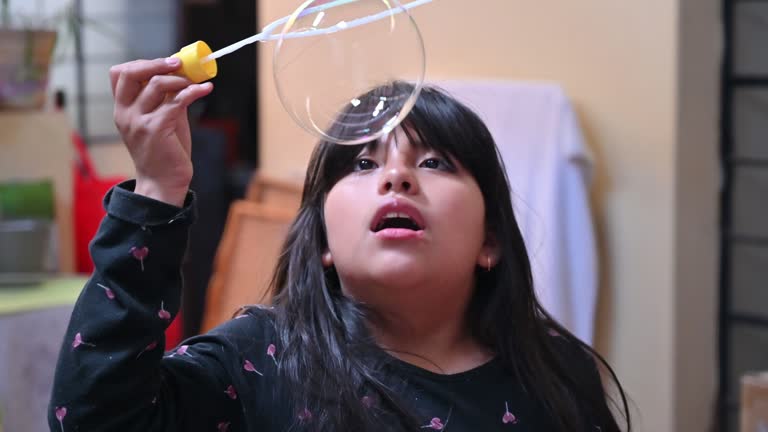 A cute little girl blowing smoke soap bubbles inside her house