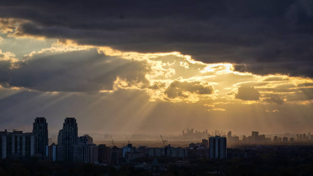 Crepuscular rays shine through dark clouds over urban skyline, when a cold weather front is approaching West Toronto. Photographed in midtown.