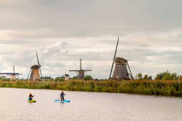 Kinderdijk, The Netherlands - September 25, 2022: Tourists enjoying an autumn day doing paddle around Windmills.Netherlands rural lanscape with windmills at famous tourist site Kinderdijk in Holland / Netherlands on sunset with a candid dramatic sky.