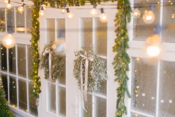 istock Christmas comfort. Christmas tree wreaths on white doors surrounded by numerous lights 2185444049