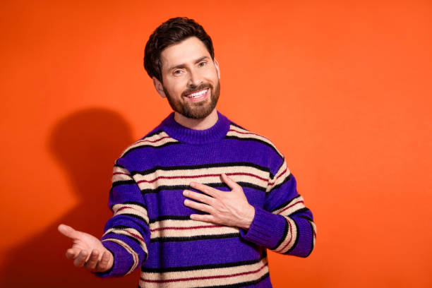 istock Friendly mature man with beard extending hand and smiling, wearing striped blue sweater, posing against vibrant orange background offering warm welcome 2185444730