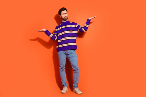 istock Full length photo of handsome young guy skeptical compare empty space dressed stylish striped purple garment isolated on orange background 2185444878