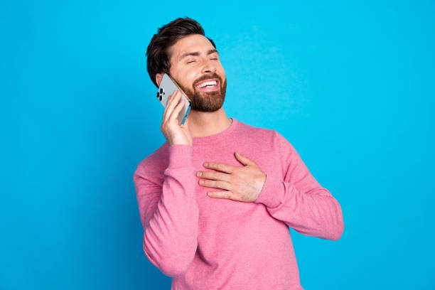 istock Joyful bearded man in pink sweater laughing while talking on smartphone against bright blue background 2185451139