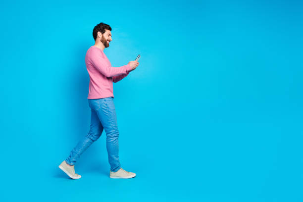 istock Confident young man walking with smartphone over bright blue background, expressing joy and casual style in trendy attire 2185451152