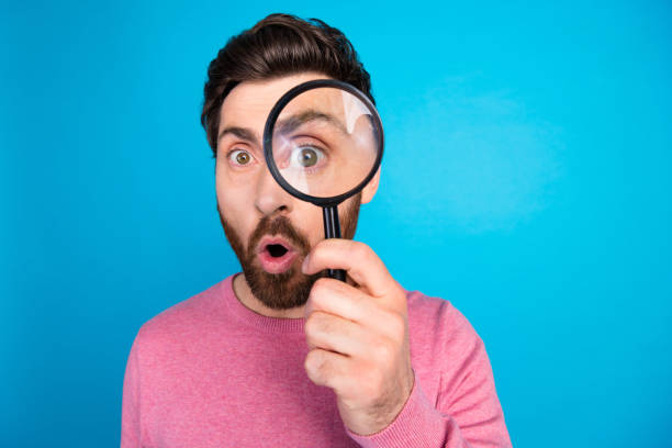 istock Curious bearded man exploring with magnifying glass against vibrant blue background, playful expression 2185451271