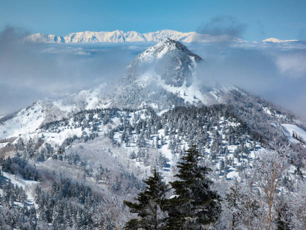 istock Jagged mountain peaks and snow covered forest surrounded by wispy layers of cloud 2185453073