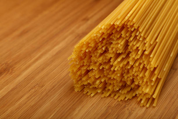 Close-up of dry spaghetti on a wooden board, perfect for cooking. Promises a tasty meal, capturing Italian simplicity and beauty. Ideal for showcasing healthy home cooking
