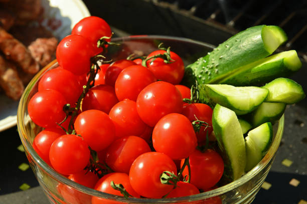 Fresh cherry tomatoes and sliced cucumbers are served in a glass bowl, offering a refreshing and healthy side dish during a barbecue gathering