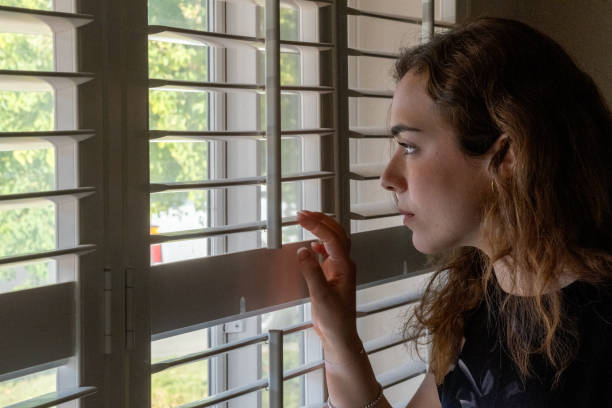 istock Serious Young woman looking outside through her home window 2185461181