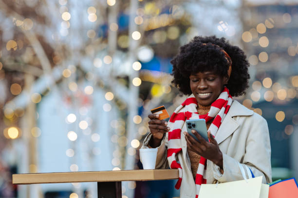 istock Young African American woman using e commerce services on smartphone during Christmastime in the city 2185463005
