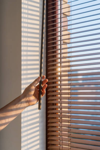 istock Hand adjusting wooden blinds to control sunlight in a bright room during morning 2185464136