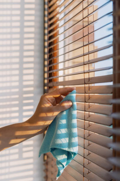 istock Cleaning wooden blinds with a blue cloth in bright sunlight, creating shadows indoors 2185464176