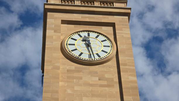 istock A tall sandstone clock tower with a gold-accented clock face stands against a partly cloudy sky, blending classic design elements with striking architectural precision. 2185477326