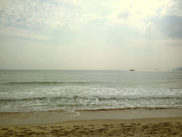 Sunny beach with waves crashing in the background. Ocean is calm and the sky is clear. The beach is empty and the waves are small