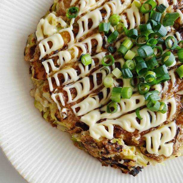 Okonomiyaki, a savory Japanese pancake made with cabbage, flour, and eggs, topped with a flavorful mix of mayo, okonomiyaki sauce, seaweed flakes, and bonito for a rich taste.