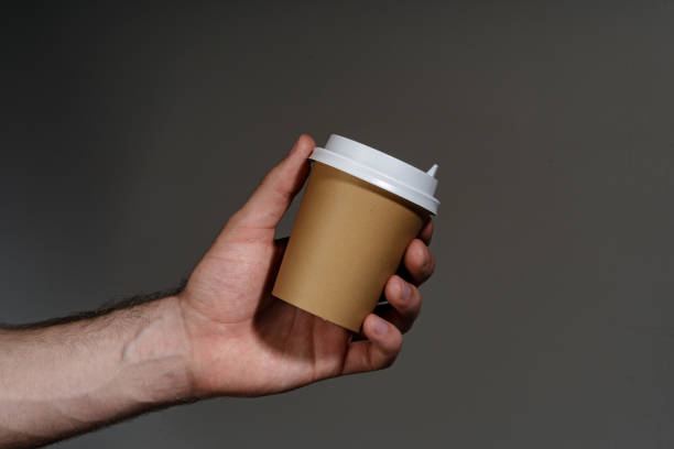 A hand holding a disposable coffee cup against a dark background