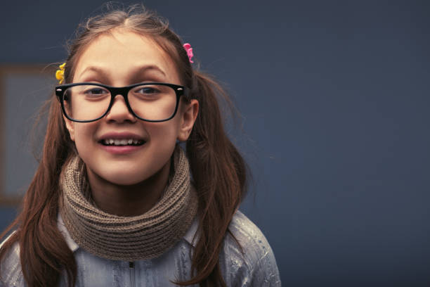 Joyful girl in stylish glasses and cozy scarf exudes confidence and innocence, radiating happiness against a vibrant blue background