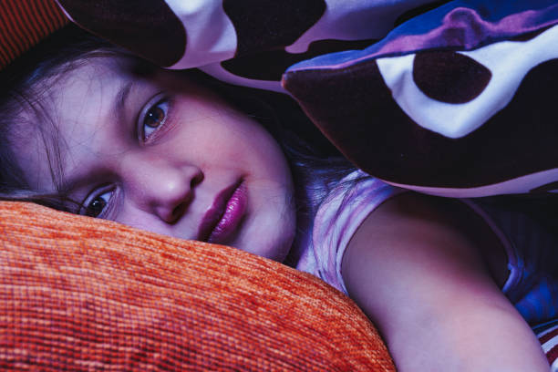 Young girl lies asleep in her bed, her face partially obscured by the covers, creating a peaceful and dreamy atmosphere