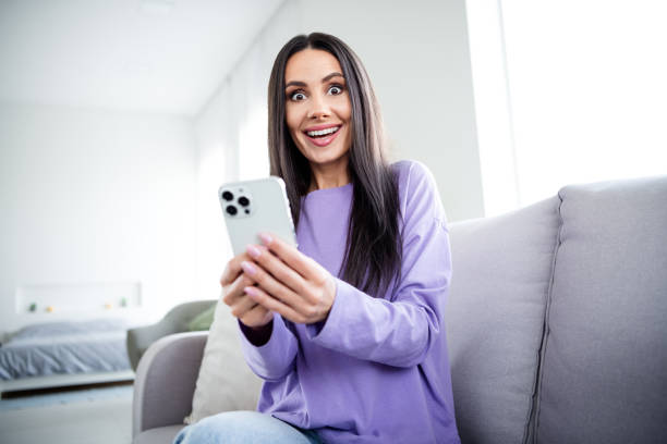 istock Young woman in stylish pullover smiling with excitement at phone indoors 2185518291