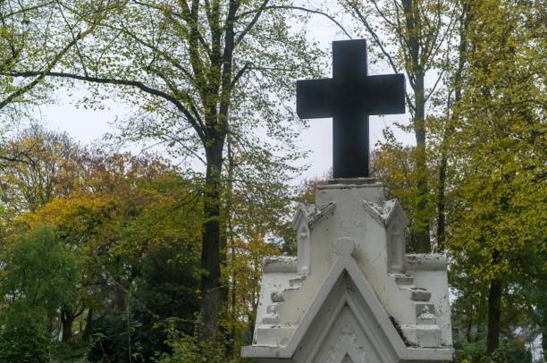 Large black cross standing on ornate white monument in cemetery during autumn