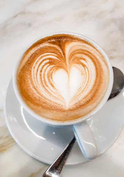 Creamy cappuccino decorated with a heart-shaped latte art design, served in a white cup on a marble table, perfect for a cozy coffee break