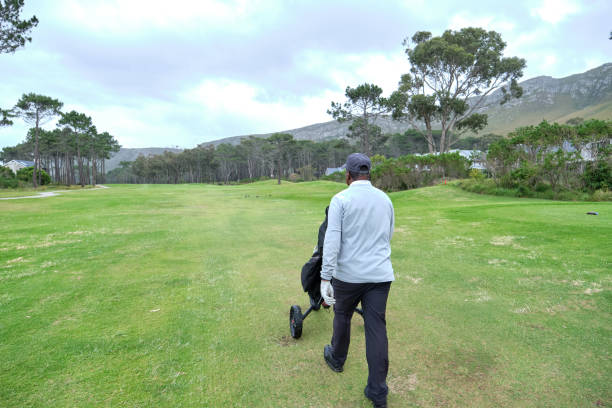 Rear shot of a golfer of African ethnicity walking down the fairway towards the green. He is enjoying a leisurely round of golf on an overcast day.