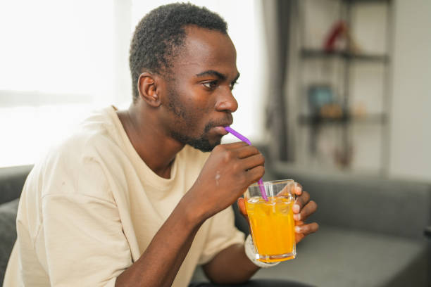 istock Black man with tooth sensitivity drinking iced drink through a straw sitting on the sofa at home 2185538013