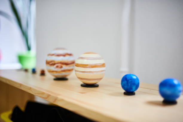 Montessori solar system model on a wooden shelf. Painted planetary spheres representing planets, arranged in size and color gradient in a preschool classroom.