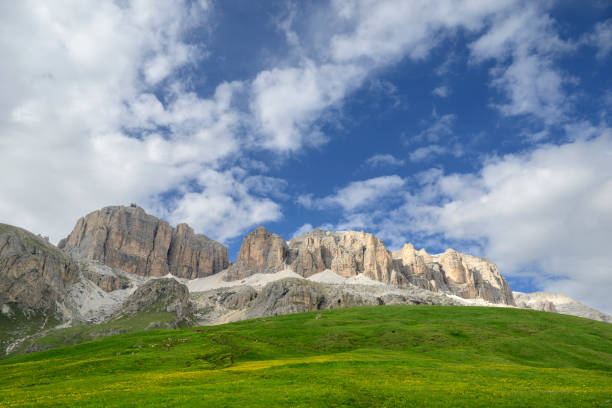 Sella group plateau-shaped massif in the Dolomites mountains  seen from the Passo Pordoi during a sprintime day in the Italian Alps. A footpath is winding through the Alpine meadow alms.