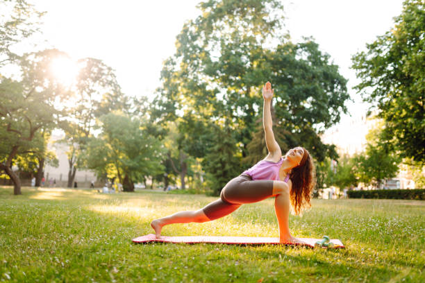 istock Young woman trainer in tracksuit changes yoga pose at public park. 2185540521