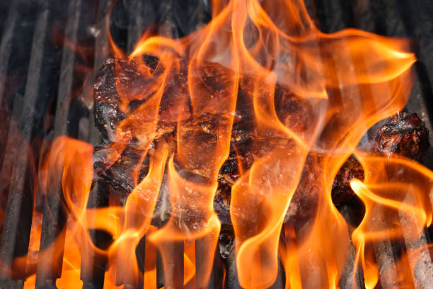 Mouth-watering meat sizzling on a barbecue grill, surrounded by flames and smoke, evoking anticipation of a delicious outdoor meal