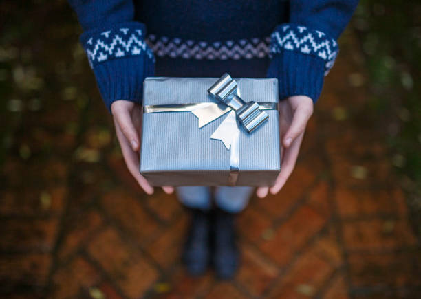Child holding christmas gift wrapped in silver paper with silver and white bow, standing on a brick pathway