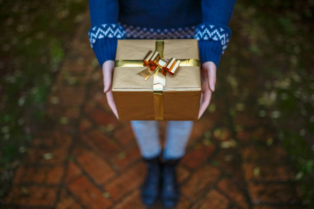 Teenager offering christmas gift wrapped in gold paper stock photo