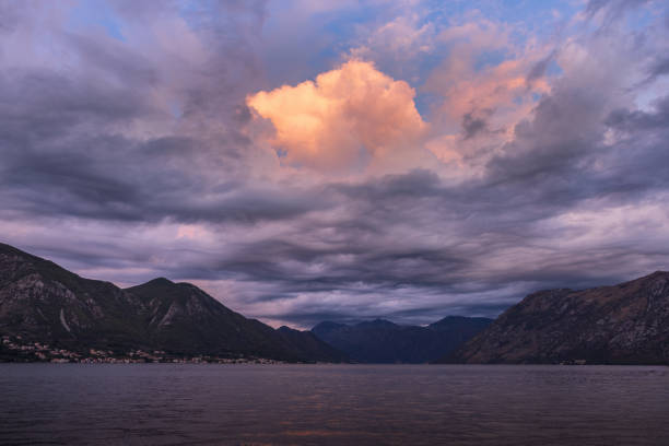 Clouds over the Bay of Kotor at dawn, with changing cloud shapes and color gradients in the sky, reflecting on the water surface, creating a mirror effect.