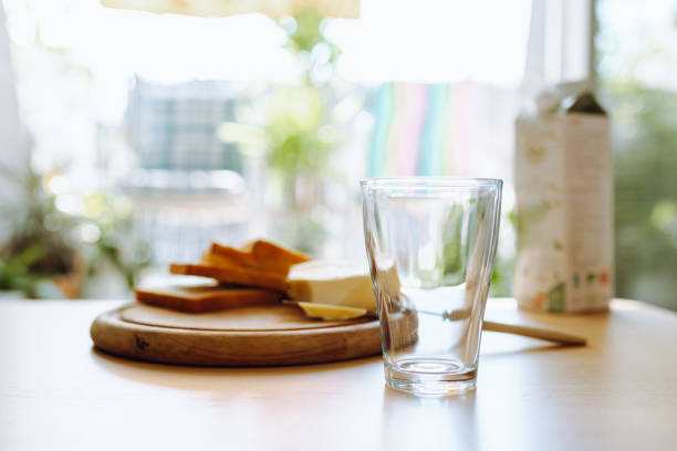 An empty glass stands on table, in background there is bread, butter, milk. Breakfast. Summer warm atmosphere of open window to terrace, simple country food
