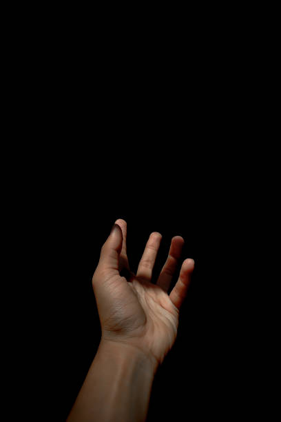 istock Male hand reaching for light in darkness on isolated black background. Selective focus on hand 2185545464