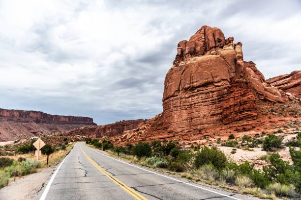 A scenic road winding through red rock formations in a desert landscape under a cloudy sky.