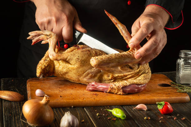 istock A skilled chef adeptly carves a whole chicken with a large knife, surrounded by fresh ingredients. The warm kitchen atmosphere highlights the culinary artistry in preparation 2185549917