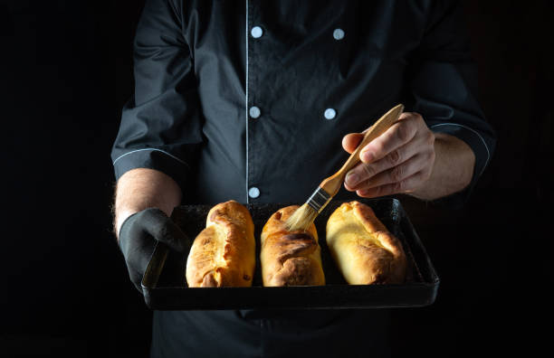 istock A skilled baker carefully brushes glaze onto three golden-brown bread rolls, showcasing their crisp texture and inviting aroma. The warm atmosphere radiates comfort and culinary passion 2185549922